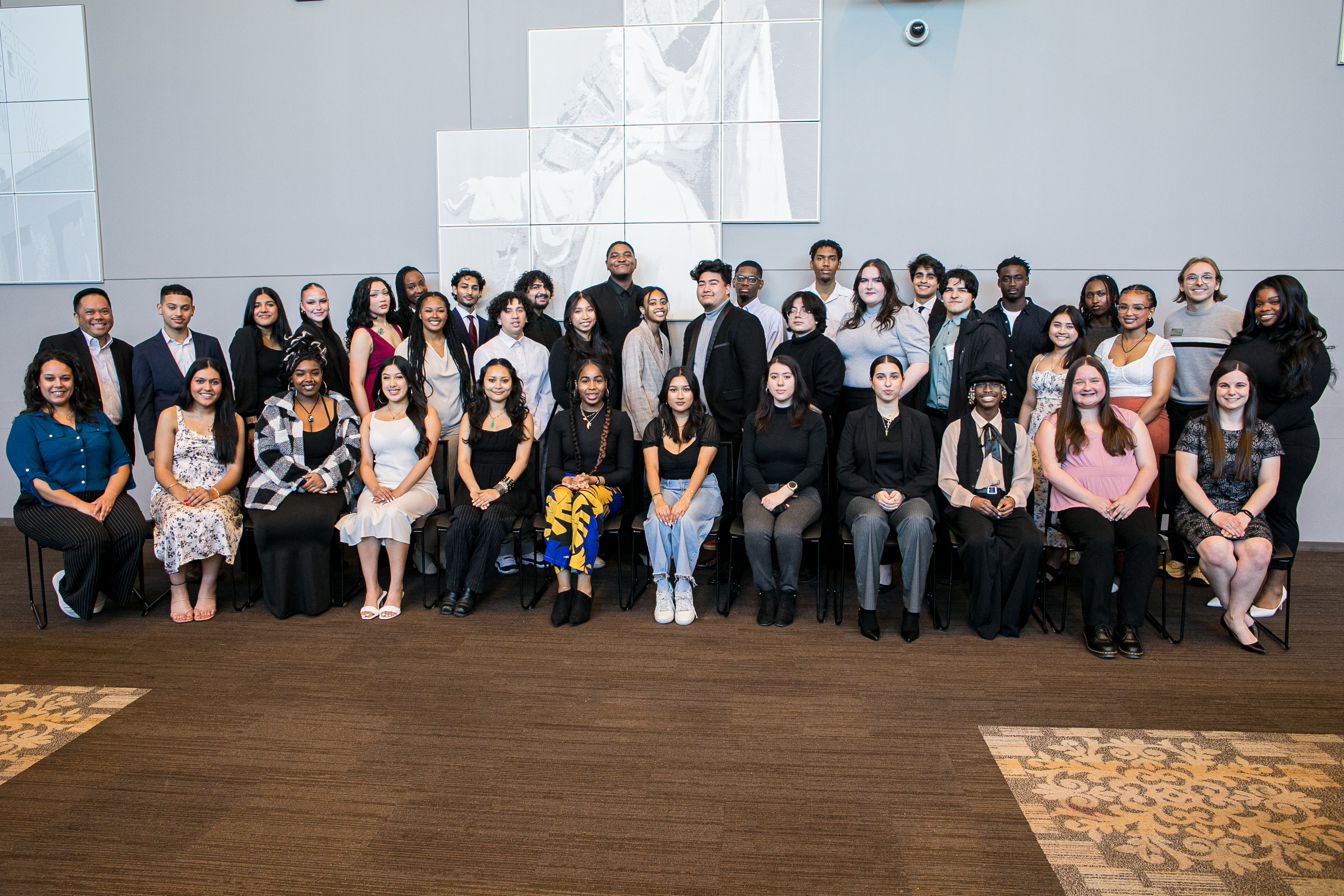 Large group of diverse Loyola University of Chicago faculty and staff for the Leadership Scholars Program, taken in a large room with half the group sitting on chairs and half standing behind them.